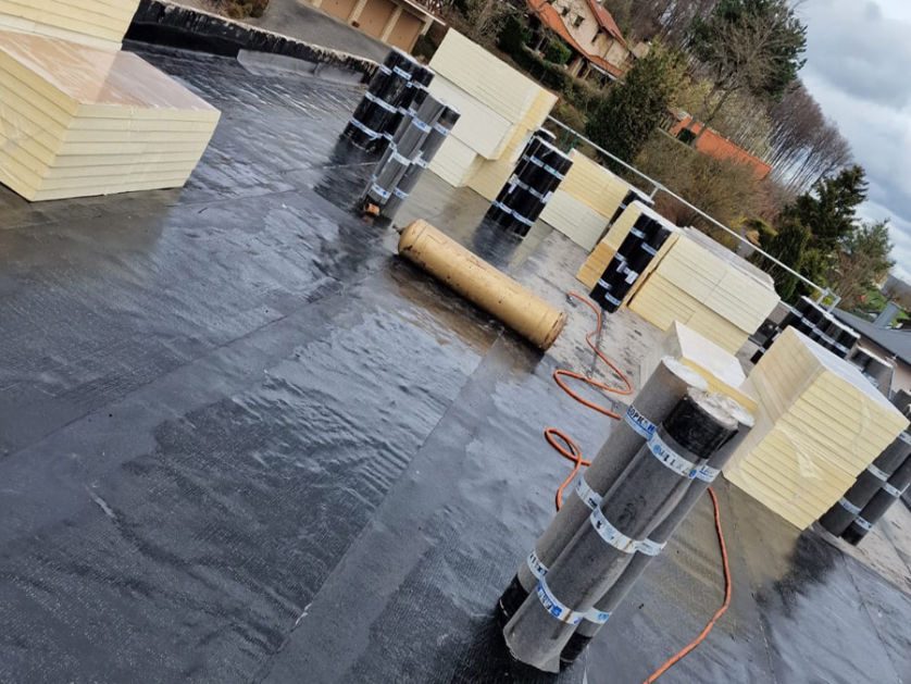 Étanchéité de toiture-terrasse en cours, rouleaux de membrane et panneaux isolants